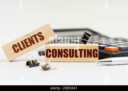 Business and finance concept. On a white background, a calculator, a pen, reports and wooden dies with the inscription - Clients Consulting Stock Photo