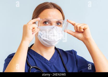 Female doctor putting on surgical face mask and medical goggle Stock Photo