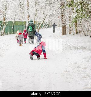 Winter, snow, park, group of young children going for walk in fresh air, one child fell on in snow Stock Photo