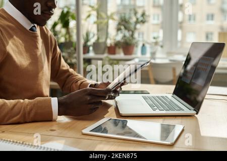 Young African American businessman examining business documents while working at table with laptop and digital tablet Stock Photo