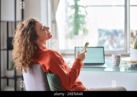 Young woman using phone relaxing taking break from remote work at home. Stock Photo