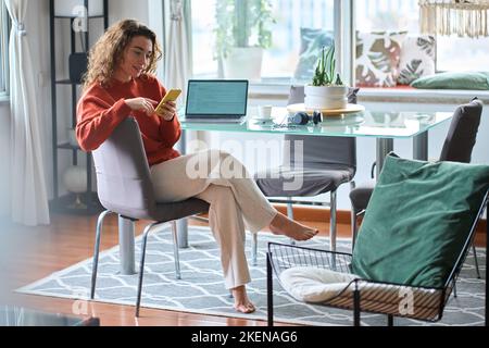 Young relaxed woman using mobile phone studying or working at home. Stock Photo