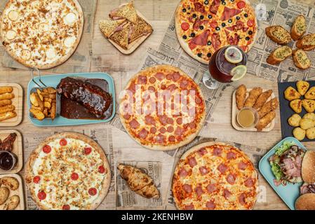 Set of fast food dishes and family pizzas with four cheeses, ham and pineapple, freshly baked sausages, barbecue ribs, buffalo chicken wings with garl Stock Photo