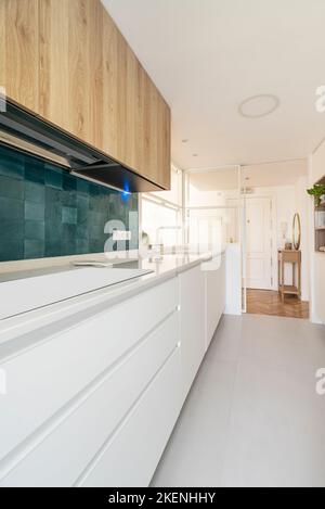 Minimalist kitchen with white base units and raw wood wall units with glossy cobalt blue tiles Stock Photo