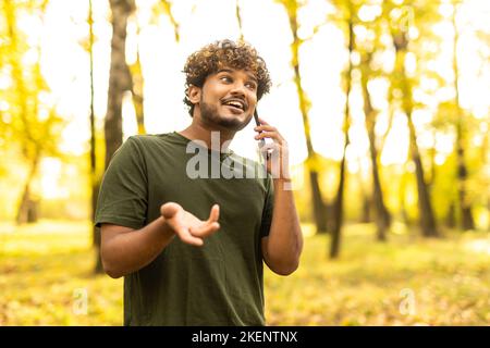 Young Indian man talking on smart phone while standing in a park outdoor summer Stock Photo