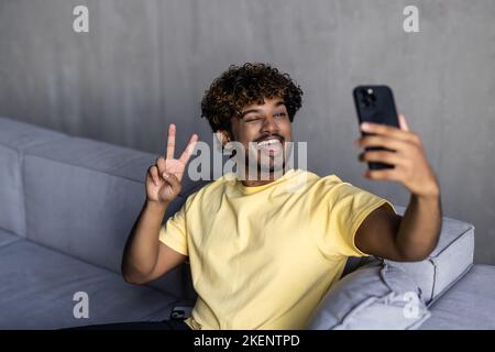 Glad to meet. Cheerful happy indian man in casual wear using smartphone app for virtual communication, holding phone in hand and waving at webcam, hol Stock Photo