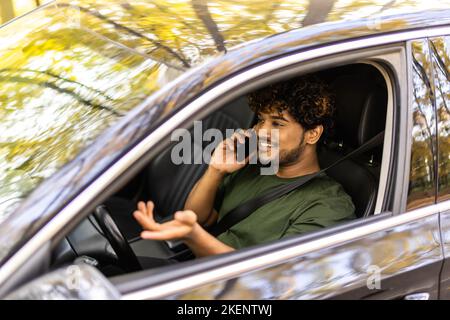 Portrait of young handsome dark-haired man driving car and speaking on mobile phone. Stock Photo