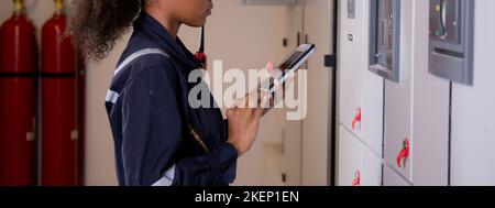 Electrical young asian woman engineer examining maintenance cabinet system electric and using tablet in control room at industrial factory, technician Stock Photo