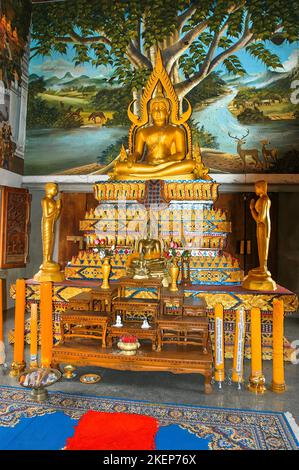 Gilded gold-coloured Buddhist altar with statue of seated Buddha in background mural with deer, Buddhist temple Wat Sri Sunthon, Thalang, Phuket Stock Photo