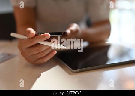 Asian female freelancer remote working at the co-working space using her smartphone and tablet, checking message on her phone. cropped shot Stock Photo