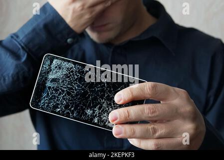 Student presenting a broken black tablet behind glass. upset man holds a out-of-use tablet or smartphone. Broken screen Stock Photo