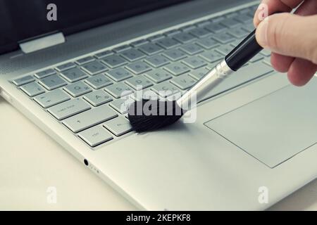 Cleaning Brush and laptop On Office desk wood table. cleaning the keyboard of the modern gray ultrabook transformer with a black brush from dust. Stock Photo
