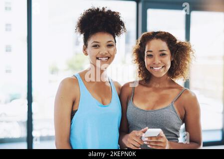 Two besties. Portrait shot of two young fit women using a phone while looking at the camera inside of a studio. Stock Photo