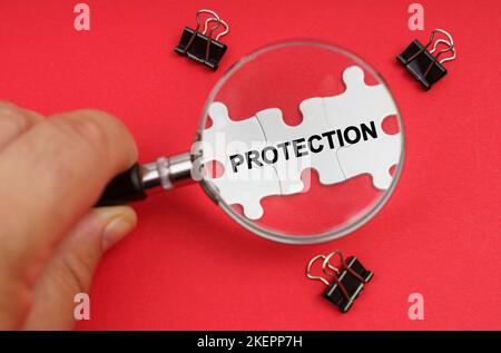 Business concept. A man looks through a magnifying glass at puzzles with the inscription - PROTECTION Stock Photo