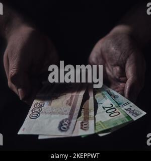 Man hands holding rubles money on a black background, close-up. Russian cash in the dirty hands of a poor man on a dark background Stock Photo