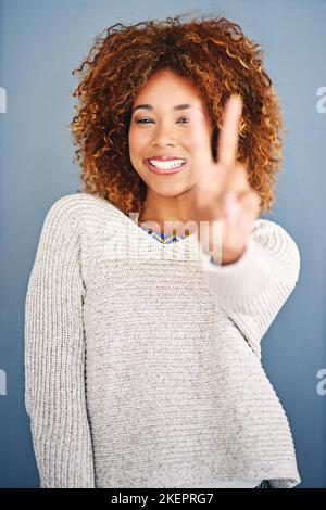 Choose peace over everything else. Studio shot of a young woman showing the peace gesture against a grey background. Stock Photo