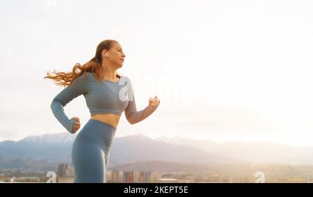 Athletic woman is running on rooftop of parking, garage on sunset background. Stock Photo