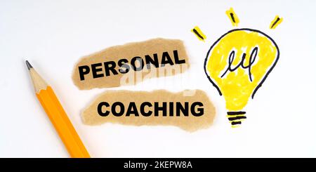 Business and finance concept. A lamp is drawn on a white sheet, there is a pencil and scraps of paper on which it is written - PERSONAL COACHING Stock Photo