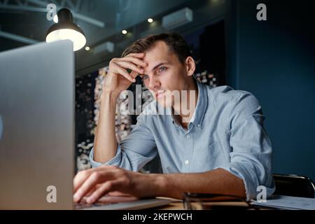 thoughtful young man looking at a laptop screen . Stock Photo