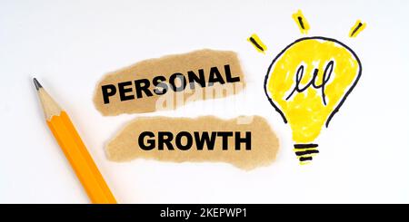 Business and finance concept. A lamp is drawn on a white sheet, there is a pencil and scraps of paper on which it is written - PERSONAL GROWTH Stock Photo