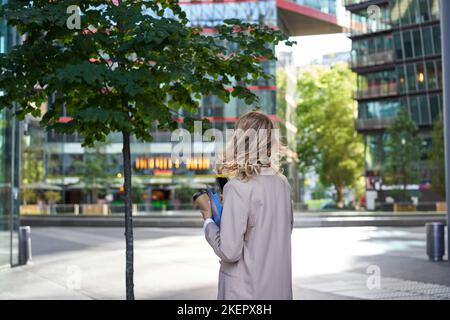 Silhouette of young business woman in beige suit, walking in city center, holding working documents and papers, standing outdoors near office Stock Photo