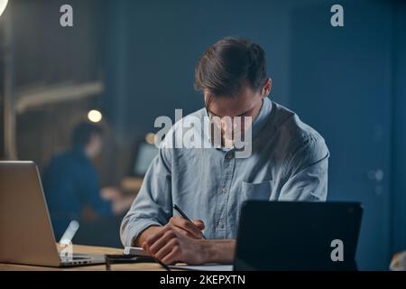 serious young entrepreneur writing something down in his weekly . Stock Photo