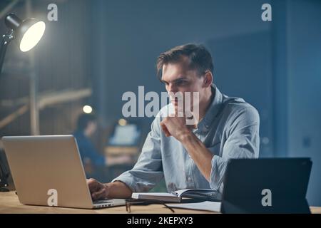 thoughtful businessman using a digital tablet and taking notes in a notebook . Stock Photo