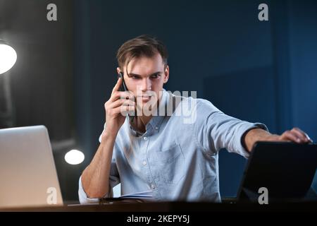 young entrepreneur talking on a smartphone while working overtime . Stock Photo