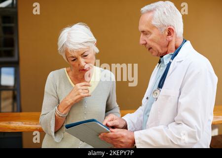 He delivers his diagnoses digitally. a senior woman discussing test results with her doctor on a digital tablet. Stock Photo