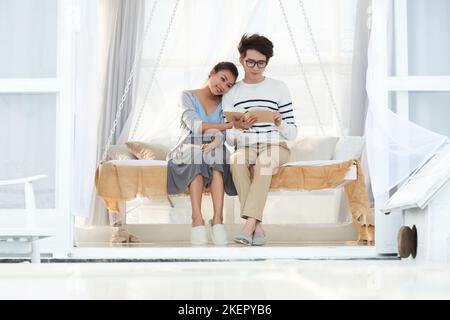 Portrait of happy young couple in love sitting on bed and reading a book Stock Photo