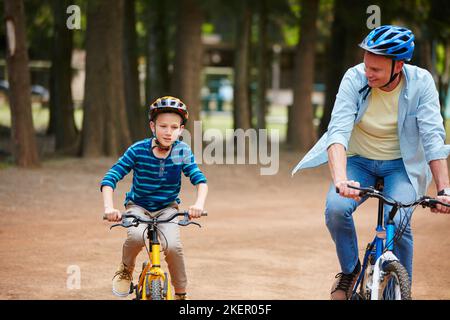 You doing great son. a father and his young son riding bicycles through a park. Stock Photo