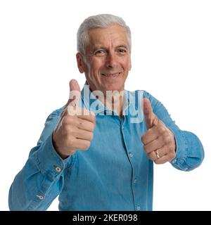 happy handsome man in denim shirt making thumbs up gesture, celebrating victory and smiling on white background in studio Stock Photo