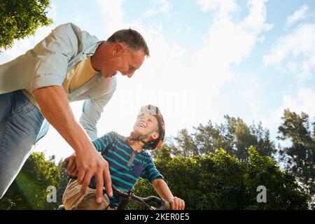 Youll be riding alone in no time. a father teaching his son how to ride a bicycle. Stock Photo