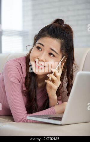 Beautiful young woman lying on sofa and calling on phone to friend Stock Photo