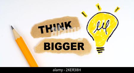 Business and finance concept. A lamp is drawn on a white sheet, there is a pencil and scraps of paper on which it is written - THINK BIGGER Stock Photo