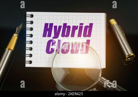 Business and Economics. On the black surface is a pen, a magnifying glass and a notebook with the inscription - Hybrid Cloud Stock Photo