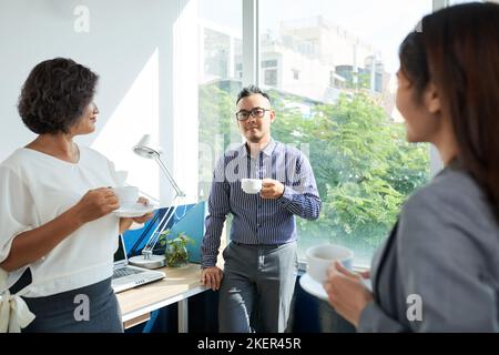Cheerful business people drinking coffee and chatting during break Stock Photo