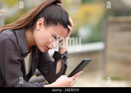 Worried teen complaining checking bad news on mobile phone in a park Stock Photo