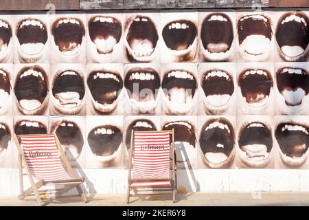 Two deckchairs in front of a wall illustrated with wide open human mouths. Brussels. Stock Photo
