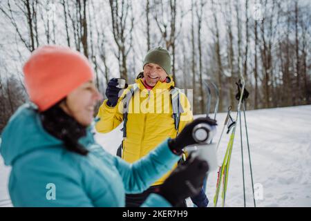 Senior couple resting and drinking hot tea from thermos in the middle of snowy nature. Stock Photo