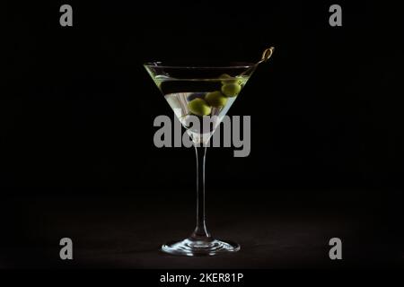 Glass of classic dry martini cocktail with olives on dark stone table against a black background. Stock Photo