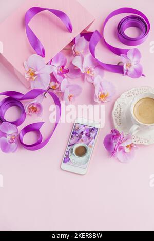 Pink home office workspace with phone and coffee cup. Social media flat lay with coffee, flowers and smartphone. Female floral workplace Stock Photo