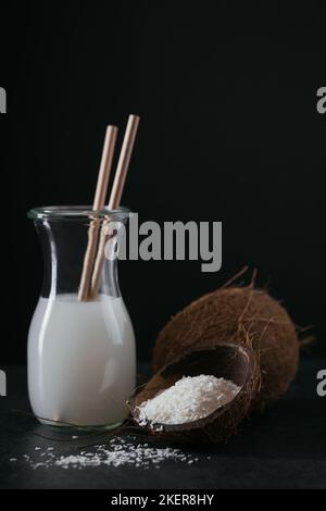 Bottle of coconut vegan milk with straws, whole coconut and flakes on black background Stock Photo