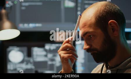 Pensive database admin brainstorming ideas in office, programming script and source code. Thoughtful man thinking about coding solution, developing app with html language late at night. Stock Photo