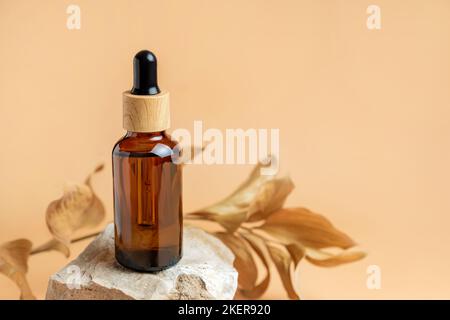 Amber dropper bottle with serum on stone podium. Beige background with dry leaves. Beauty concept for face and body care. Skincare products, natural c Stock Photo