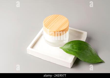 Moisturizing cream in frosted glass jar packaging on cocnrete tray on gray background. Skin care concept. Stock Photo