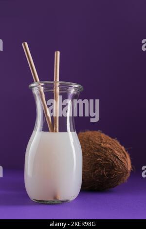 Bottle of coconut vegan milk with strews and whole coconut on a purple background. Healthy lifestyle concept. Stock Photo