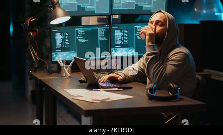 Hacker programmer coding system late at night, using virus to produce computer malware and error. Data developer stealing information from software app, working with multiple monitors. Stock Photo