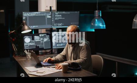 Software engineer typing source code on multiple monitors, displaying terminal window with html language. Programming cloud computing interface on laptop to develop system. Handheld shot. Stock Photo