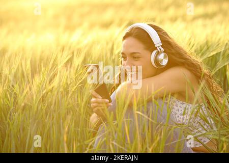 Happy woman at sunset wearing headphones listening to music from smart phone in a wheat field Stock Photo